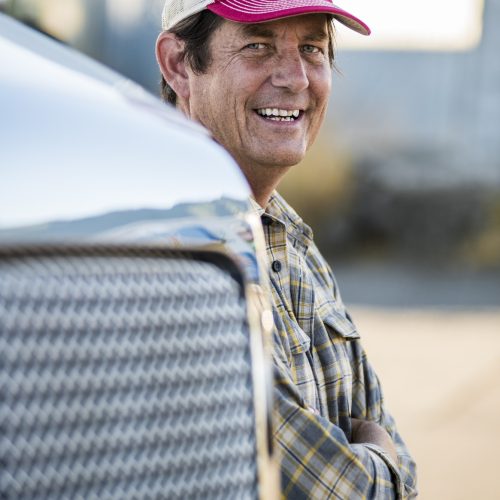 Caucasian man truck driver with his truck parked in a lot at a truck stop.